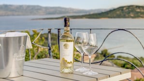 A bottle of wine and two glasses on a table with a scenic view of a lake and hills in the background. - Villa Maria - 3bdr with 2 bathrooms (Palau)
