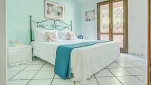 A bedroom with a bed, a nightstand, a window, and a door. - Villa Maria - 3bdr with 2 bathrooms (Palau)
