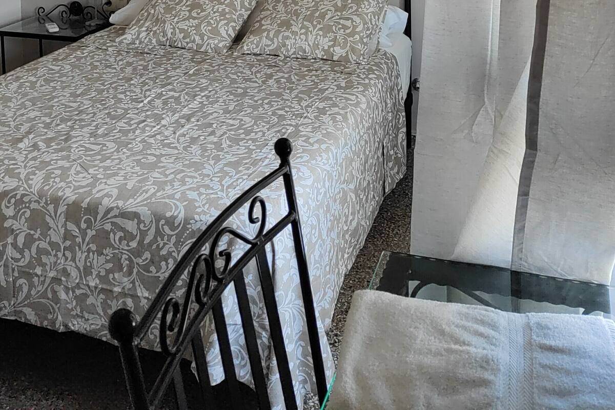 A bedroom with a bed, a nightstand, a lamp, a curtain, and a window.