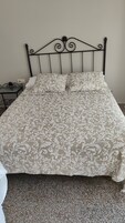 Una cama con colcha estampada, cabecera de metal y una mesita de noche con lámpara.