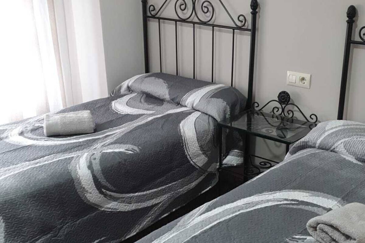 A bedroom with two beds, a metal headboard, a bedside table, a painting on the wall, and a window with curtains.