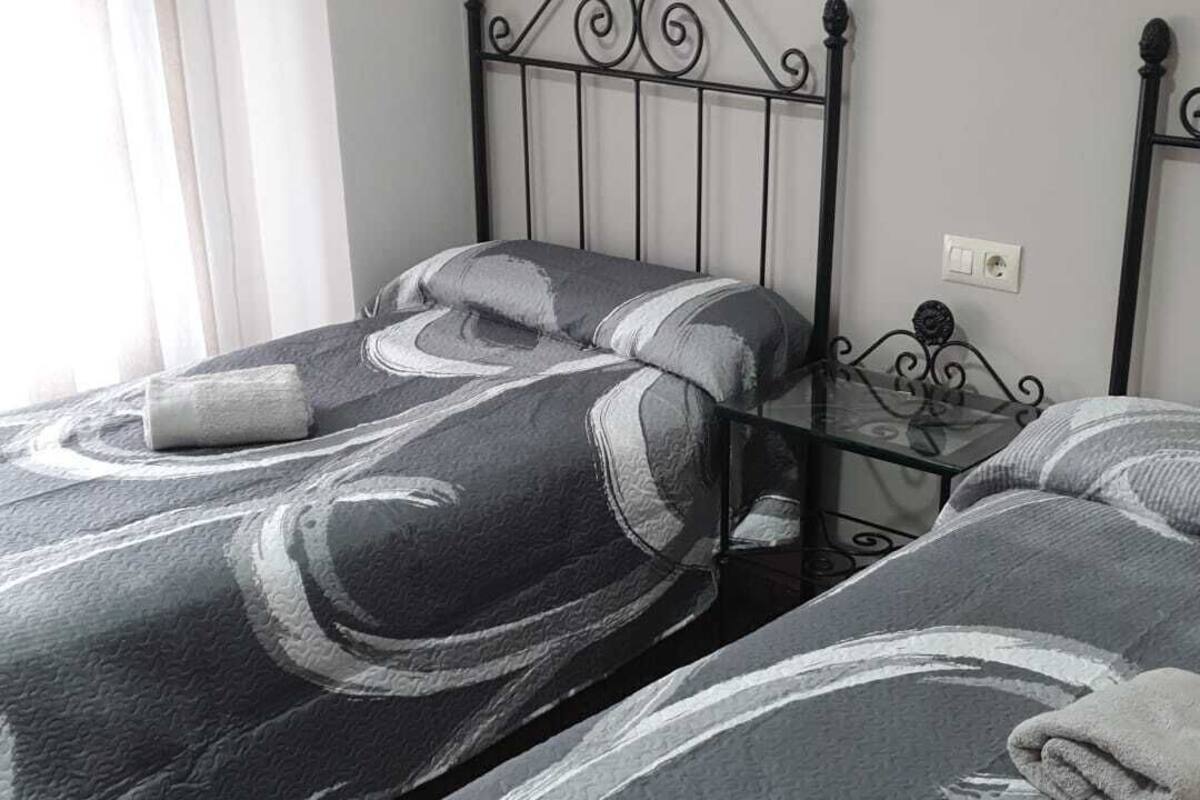A bedroom with two beds, a metal headboard, a painting on the wall, and a window with curtains.