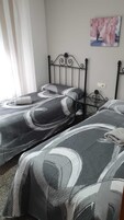 Un dormitorio con dos camas, cabeceros de metal, un cuadro en la pared y una ventana con cortinas.