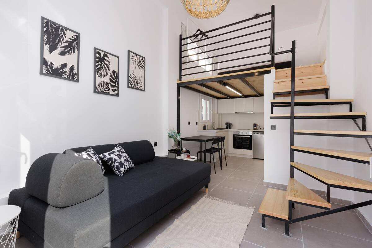 A modern living room with a black sofa, a staircase, and a kitchen in the background.