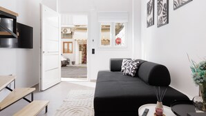Een moderne woonkamer met een zwarte bank, een houten bankje en een kleine tafel met een afstandsbediening.