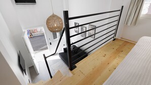 Een moderne slaapkamer met houten vloer, een zwart metalen hekwerk en een wit bed, met uitzicht op buiten.