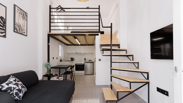 Een modern appartement met een zwarte bank, een trap met houten treden, een keuken op de achtergrond en een eethoek.
