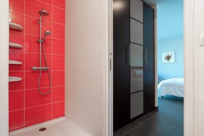 Une salle de bain avec un mur de douche recouvert de carreaux rouges, une baignoire blanche et un placard noir.