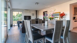 Un espace de repas moderne, avec une grande table et des chaises, un vase rempli de fleurs et une vue sur l’extérieur.