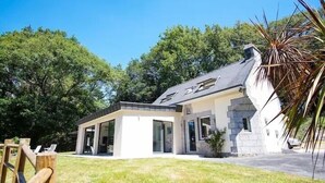 Une maison moderne avec une façade en pierre, de grandes fenêtres en verre et un toit en pente.