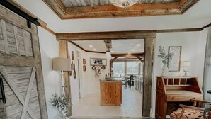 Un hall d’entrée spacieux, doté d’un parquet en bois, d’un lustre et d’une porte de grange au style rustique.