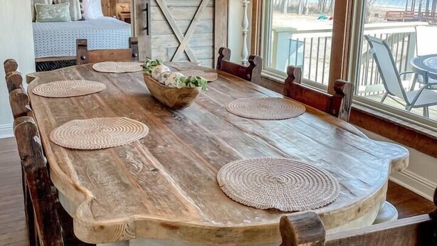Une salle à manger rustique avec une grande table en bois, des sets de table en fibres tressées et un lustre.