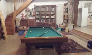 A room with a pool table, bookshelves, a staircase, and a kitchen area. - Large Landes house with swimming pool, very quiet, south of DAX (Saugnac-et-Cambran)