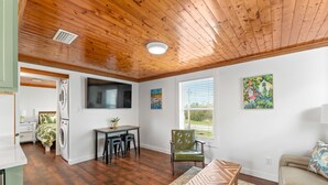 A compact living space with a wooden ceiling, a dining area with a table and chairs, a sofa, and artwork on the walls. - Cozy Cottage in the Heart of Gulf Shores (Gulf Shores)