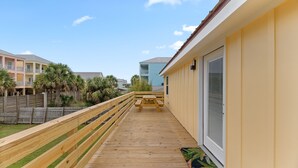 A wooden deck with a picnic table, a wooden fence, and a building with a sliding glass door. - Cozy Cottage in the Heart of Gulf Shores (Gulf Shores)