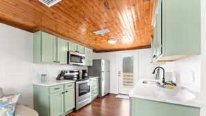 A compact kitchen with green cabinets, a microwave, a refrigerator, and a sink. - Cozy Cottage in the Heart of Gulf Shores (Gulf Shores)