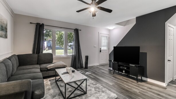 Una sala de estar moderna con un sofá modular, una mesa de centro, un televisor de pantalla plana y un ventilador de techo.