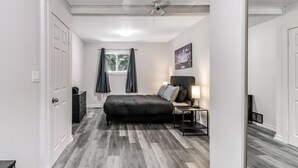 Un dormitorio con cama, mesita de noche, lámpara, ventana con cortinas y ventilador de techo.