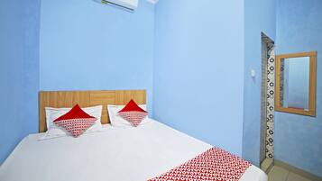 Ein Hotelzimmer mit einem Bett, zwei Kissen, einer roten und weißen Decke mit Muster sowie einem Holz-Kopfende und einer Wand-Klimaanlage.