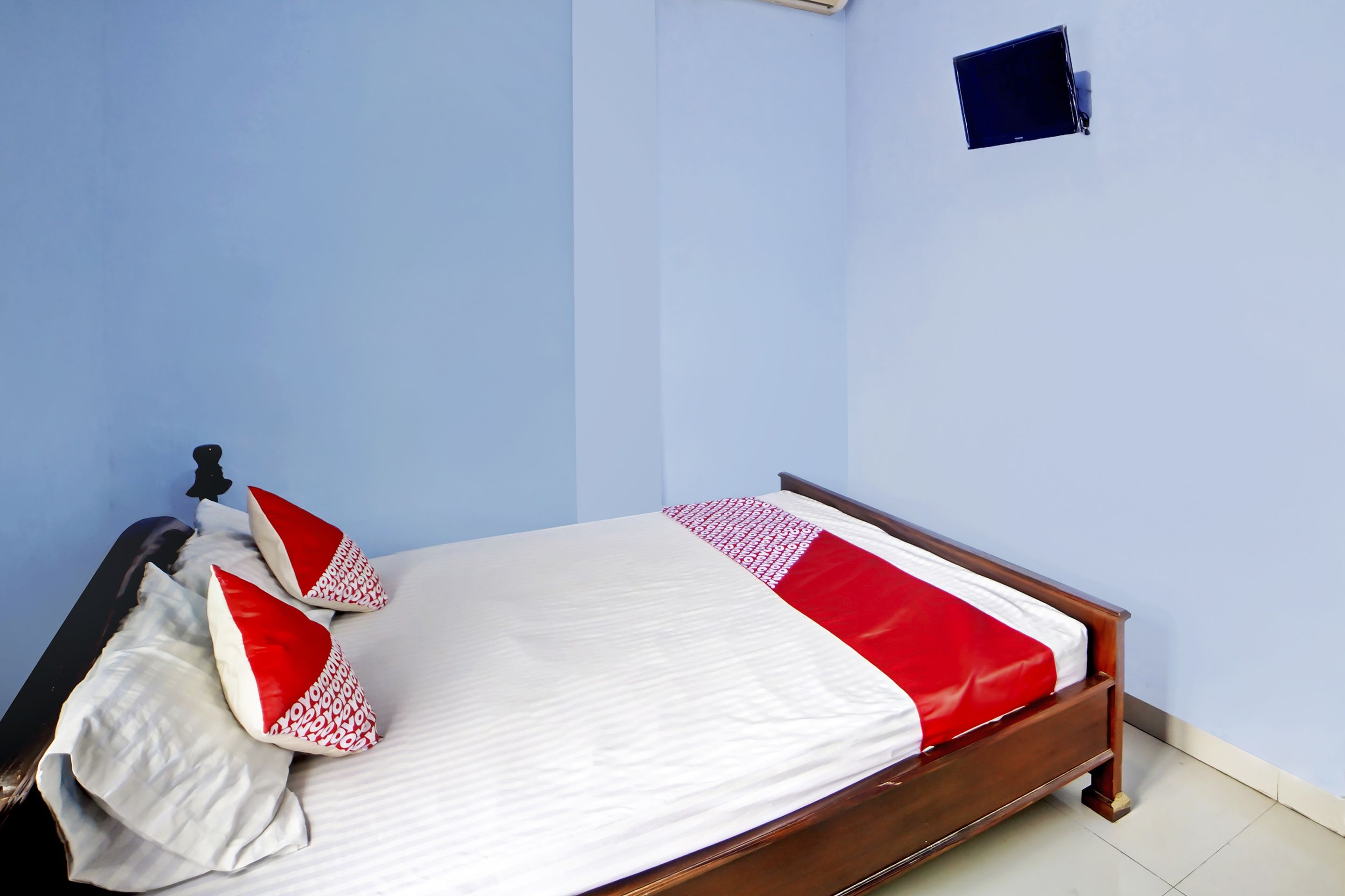 Un lit simple avec un cadre en bois, une literie blanche et des touches de couleur rouge.
