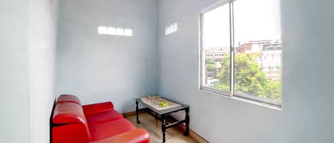 A room with a red sofa, a small table with a lace tablecloth, and a window with a view of buildings and trees.