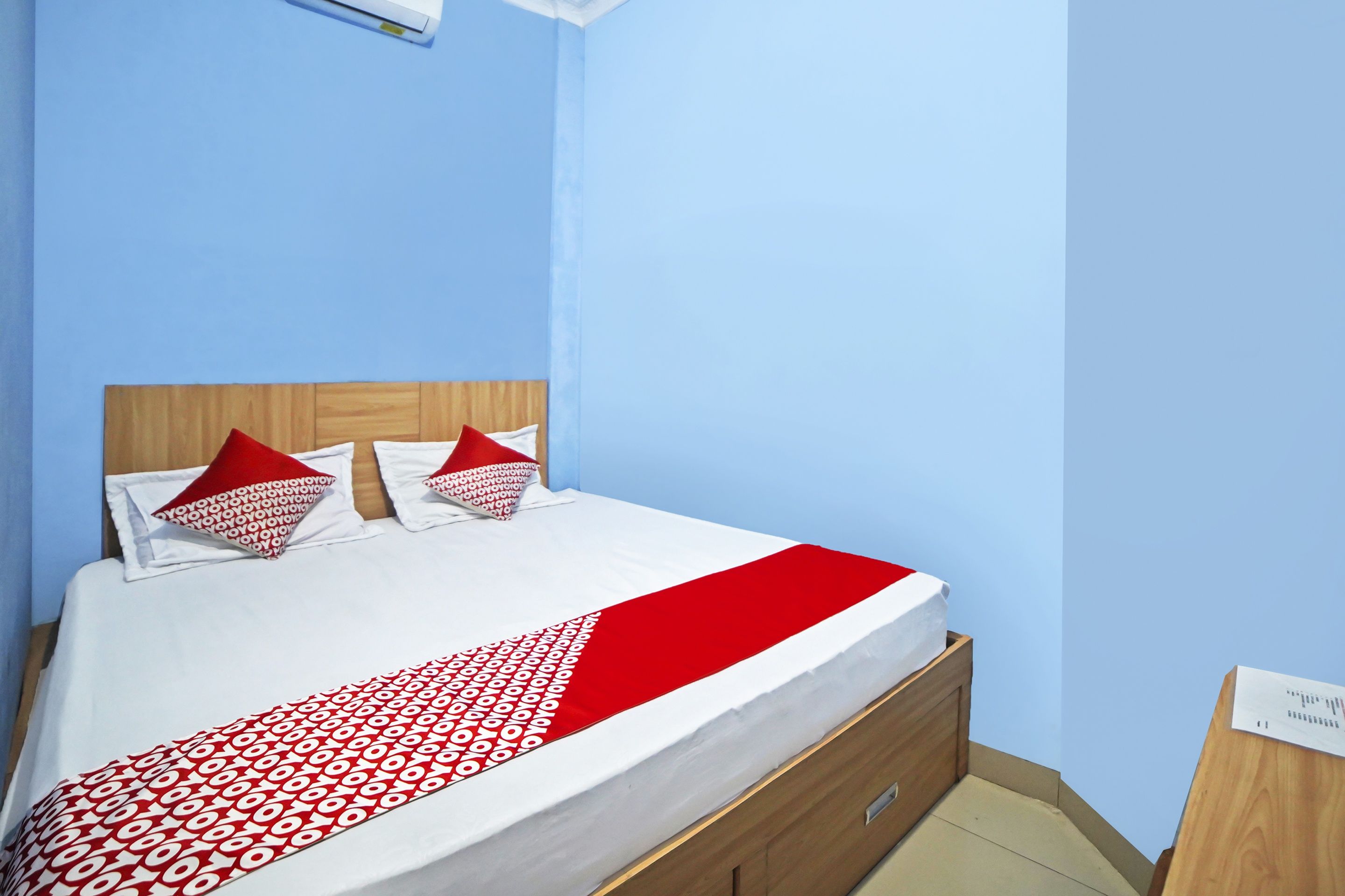 Een bed met een deken met een wit en rood patroon, twee kussens met een rood-wit ontwerp en een houten hoofdbord.