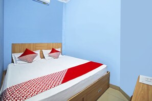Una cama con colcha blanca y roja estampada, dos almohadas con diseño rojo y blanco, y un cabecero de madera.