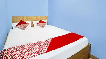 A bed with a white and red patterned bedspread, two red pillows, and a wooden headboard in a room with light blue walls.