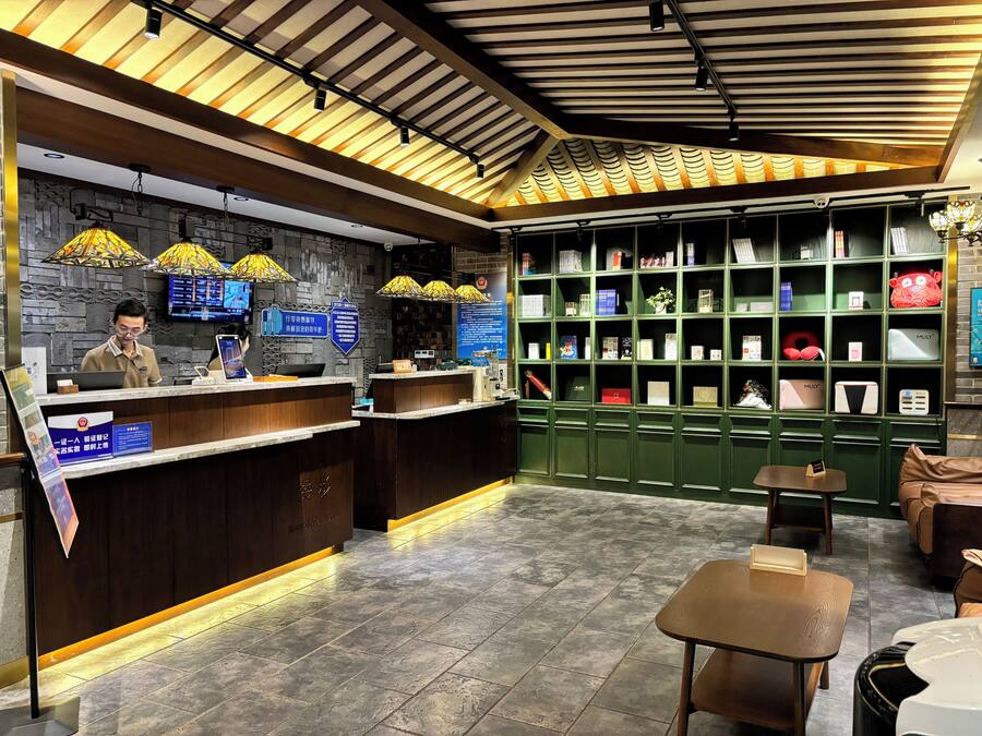 Un área de recepción con un mostrador de madera, una estantería verde con diversos objetos y un espacio de asientos con una mesa y sillas.