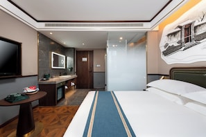 Una camera d'albergo con un letto, una scrivania con televisione, un bagno e un'opera d'arte appesa al muro.