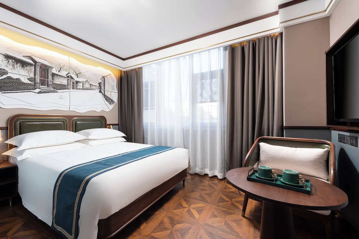 A hotel room with a large bed, a desk with a chair, a television, and a painting on the wall.