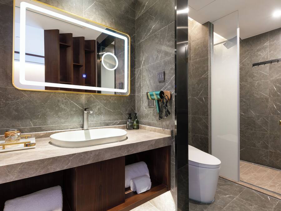A modern bathroom with a large mirror, a round vanity, a glass shower enclosure, and marble walls.
