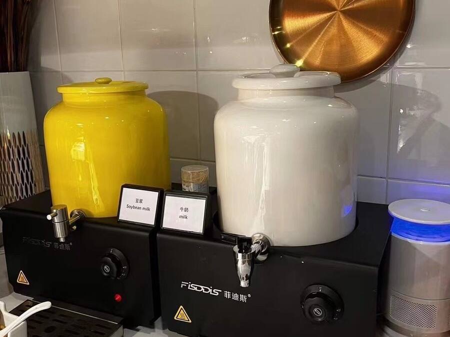 Eine Küchenzeile mit zwei Fissodys-Milchspendern, einer für Sojamilch und einer für Kuhmilch, sowie einem großen weißen Behälter.