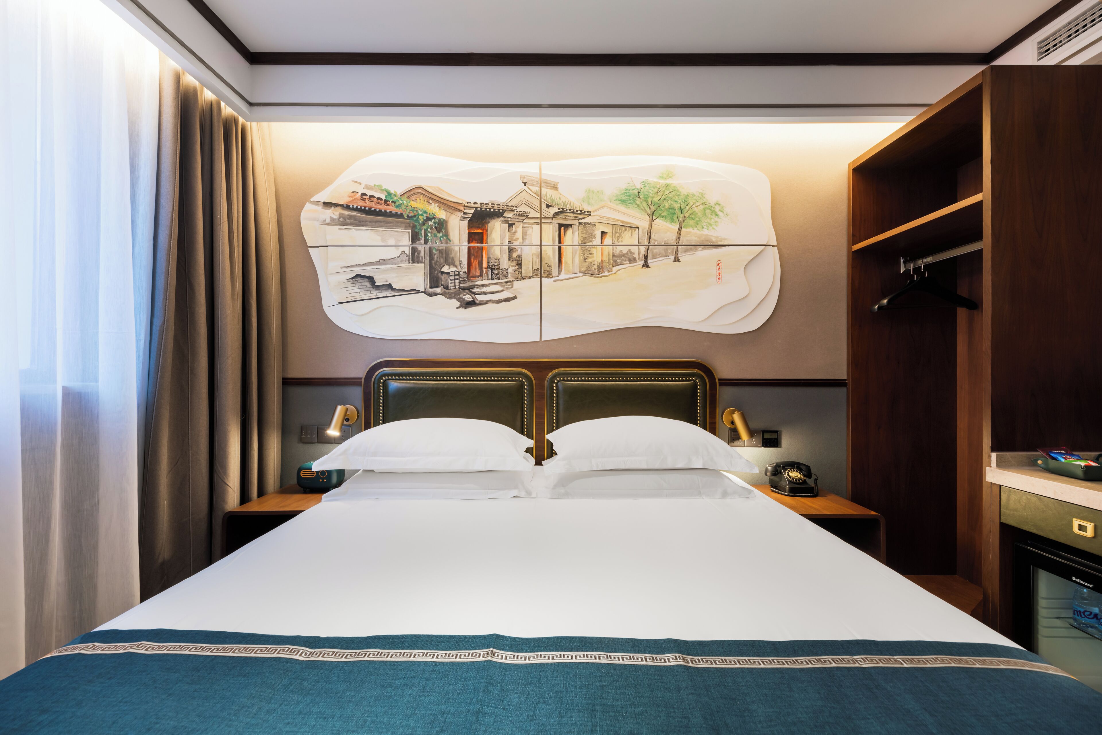Habitación de hotel con cama, mesita de noche, teléfono, espejo y un cuadro en la pared.