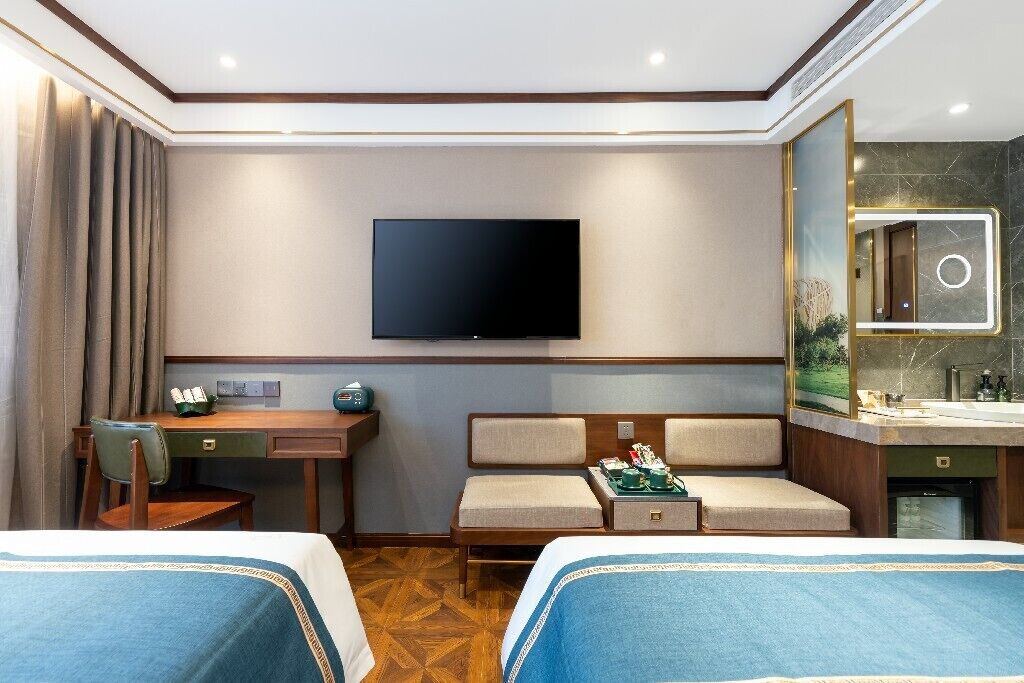 A hotel room with two beds, a desk, a chair, a television, and a bathroom with a mirror.