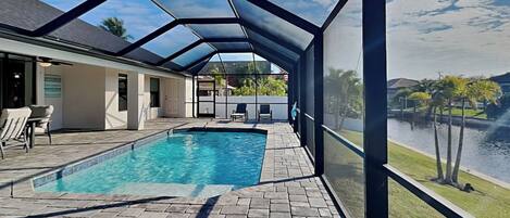 A covered swimming pool with a view of a lake and palm trees.