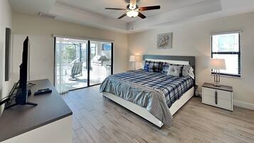 A bedroom with a bed, a desk, a television, a ceiling fan, and a sliding glass door leading to an outdoor area.