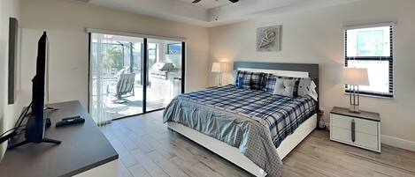 A bedroom with a bed, a desk, a television, a ceiling fan, and a sliding glass door leading to an outdoor area.