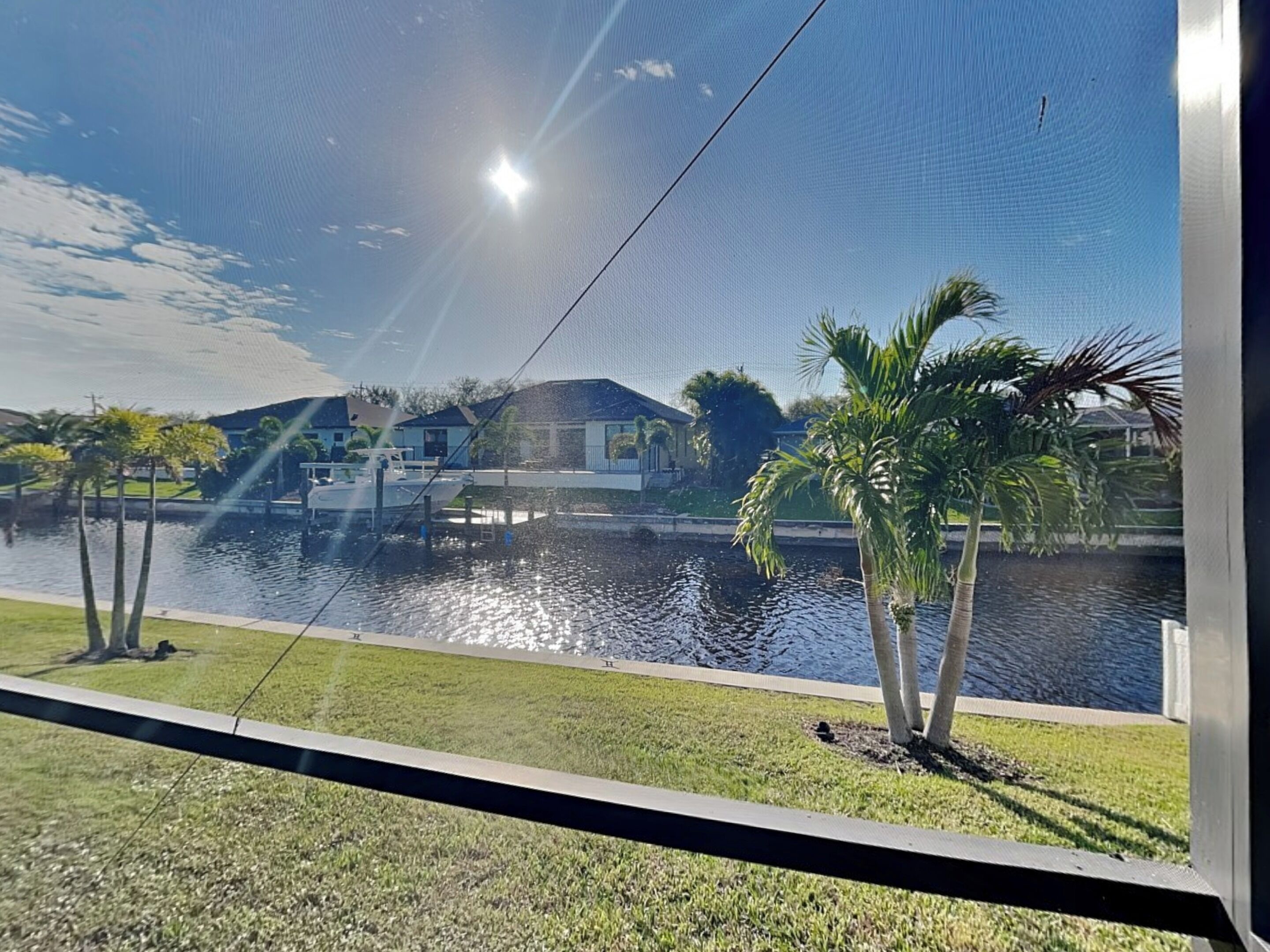 A view of a residential area with a body of water, palm trees, and houses in the background.