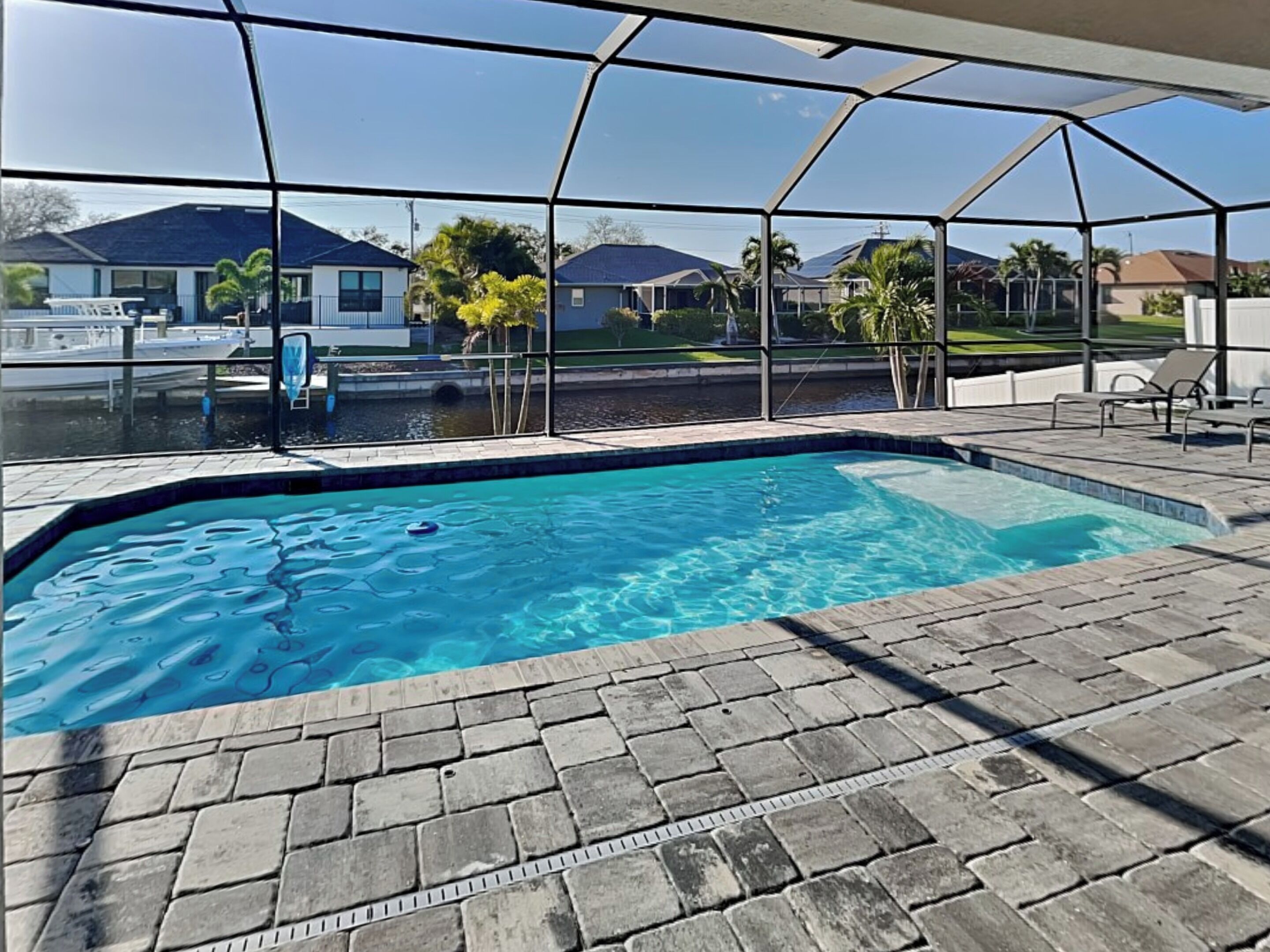 Une piscine à l’eau d’un bleu cristallin, entourée d’une terrasse dallée et d’un espace couvert équipé de chaises.