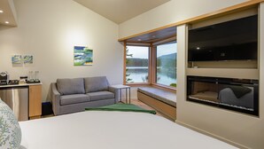 Moderni hotellihuone, jossa on sänky, sohva, pieni pöytä, televisio ja ikkuna, josta avautuu näkymä järvelle.