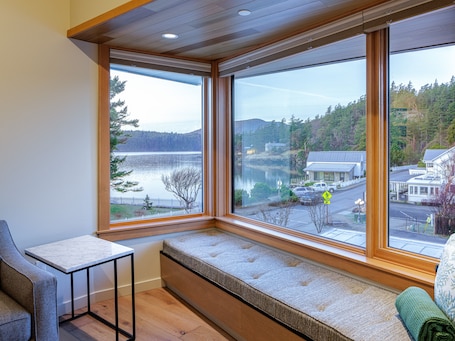 A room with a large bay window overlooking a lake, a bench, and a table.