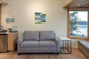 Un salon moderne avec un canapé gris, une petite table et une fenêtre donnant sur un lac.