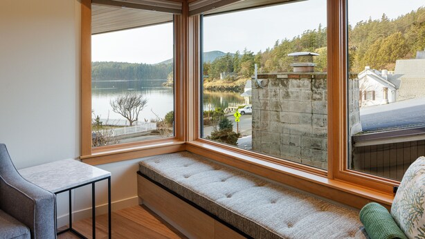 A room with a large window overlooking a lake, a bench, and a small table. - Sucia - Dramatic Eastsound Bay View (Eastsound)