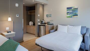 Een moderne hotelkamer met een bed, nachtkastje en een kitchenette.