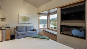 A modern bedroom with a large bed, a sofa, a TV, and a window with a view of a lake. - Sucia - Dramatic Eastsound Bay View (Eastsound)