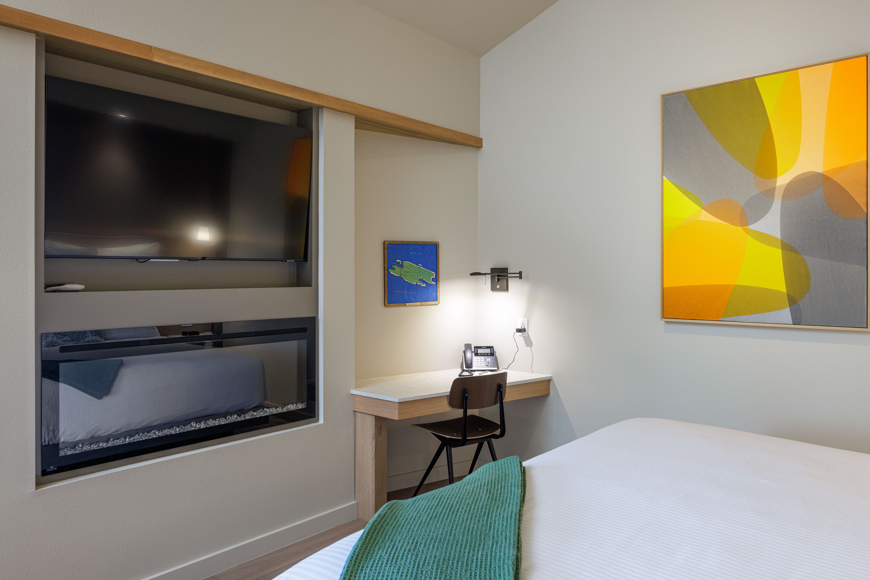 A hotel room with a bed, a desk, a chair, a window, and a wall-mounted artwork.
