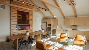 A modern kitchen with wooden cabinets, a dining area with a wooden table and chairs, and a large window allowing natural light. - Matia - Luxurious Night’s Sleep (Eastsound)