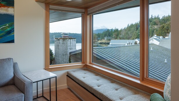 A room with a large window overlooking a residential area, a bench, and a small table. - Matia - Luxurious Night’s Sleep (Eastsound)