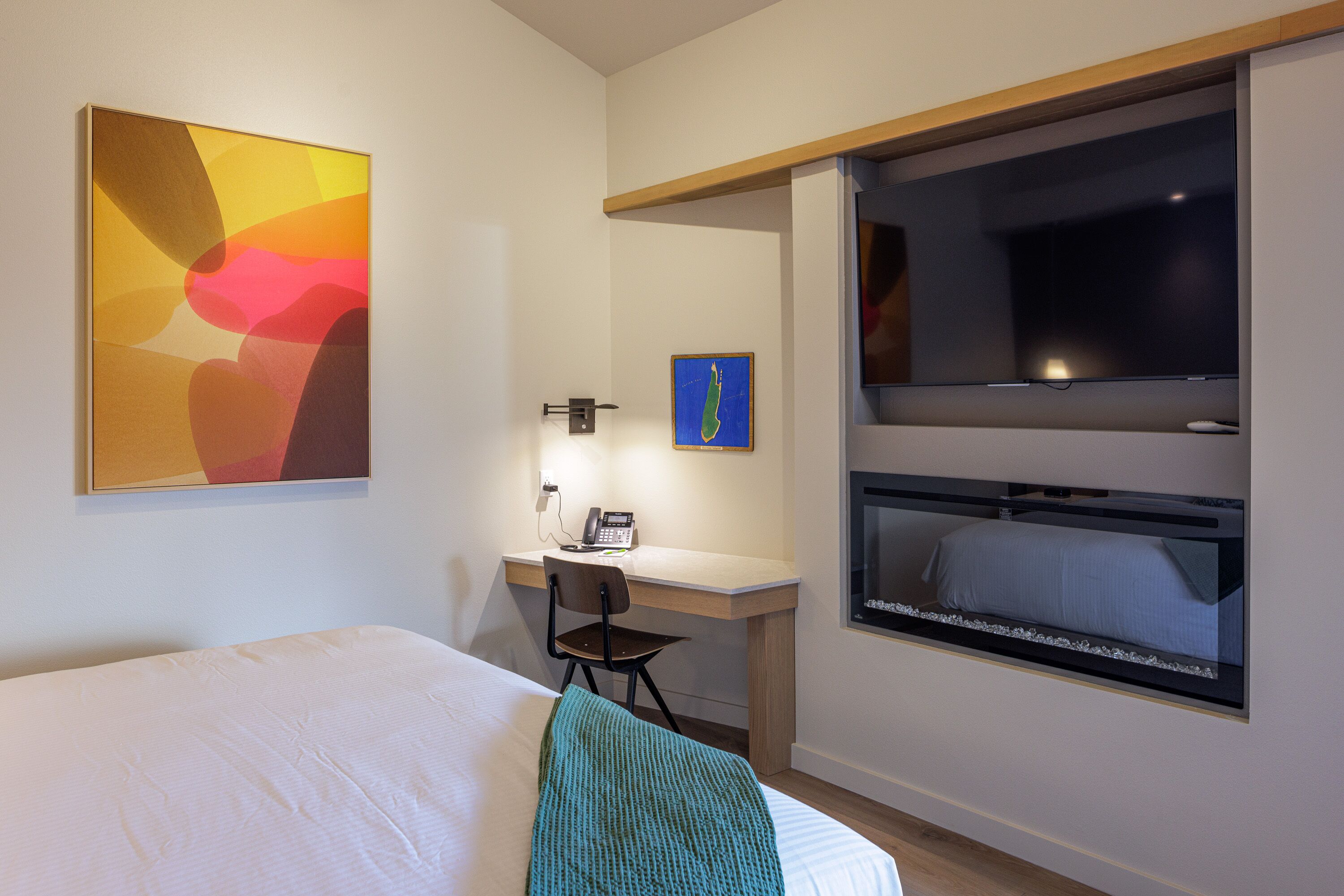A hotel room with a bed, a desk with a chair, a television, and artwork on the walls.
